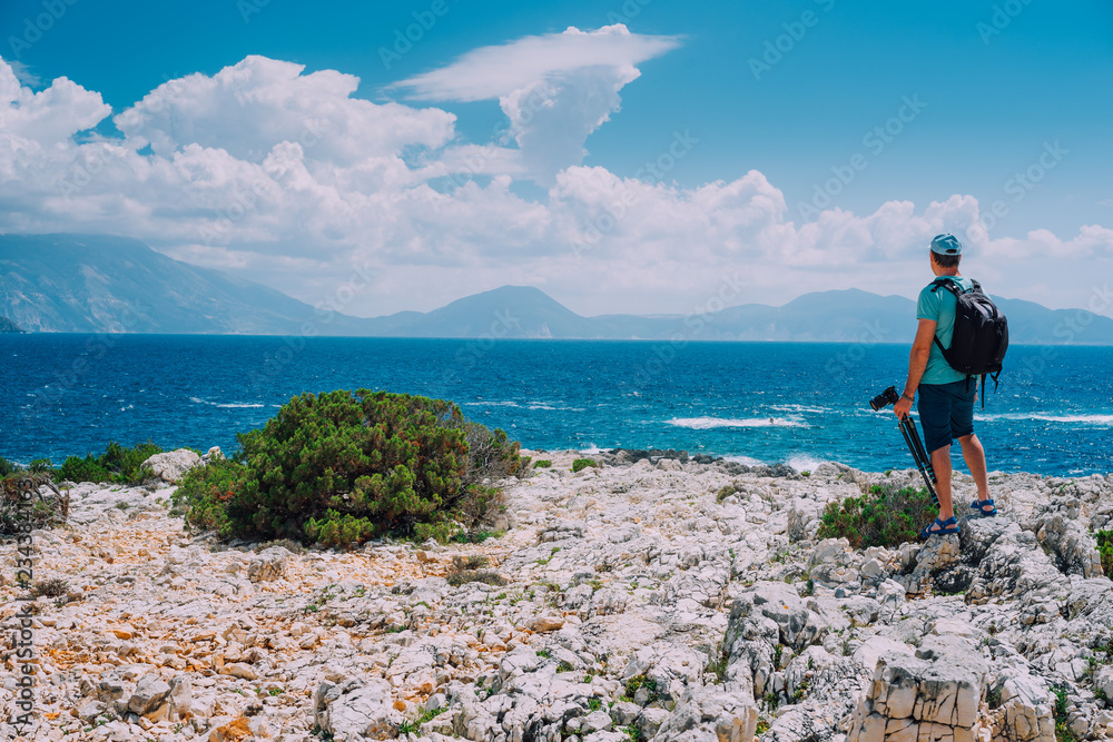 Male tourist with camera admiring breathtaking cloud scenery over the mountain range at the Mediterranean sea coast. Sunning outdoor scene of Ionian Islands, Kefalonia, Greece