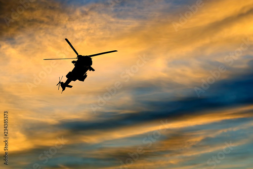 Silhouette of a flying helicopter against the bright evening sky