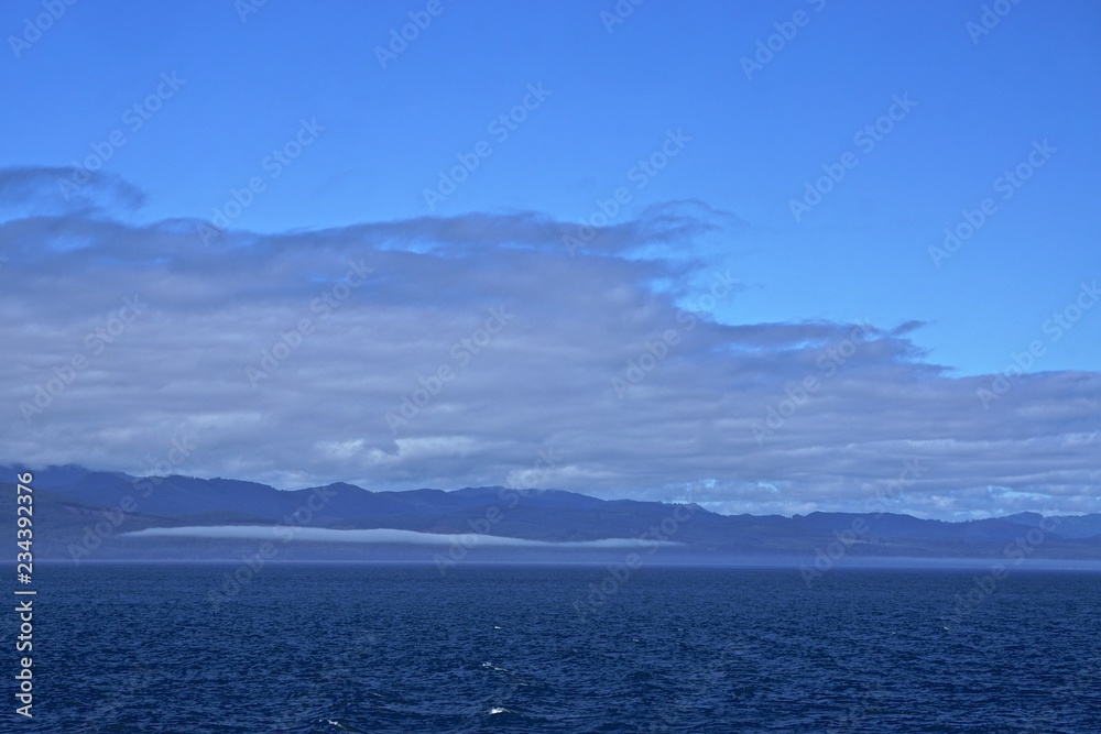 Morning at sea: Clouds and fog in a deep blue sky over Alaskan islands in the North Pacific Ocean.