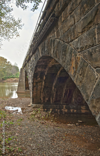 A skewed arch stone bridge in Western Pennsylvania stretching across a river. © StudioStoltz