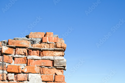 part of a crumbling brick wall against a clear blue sky