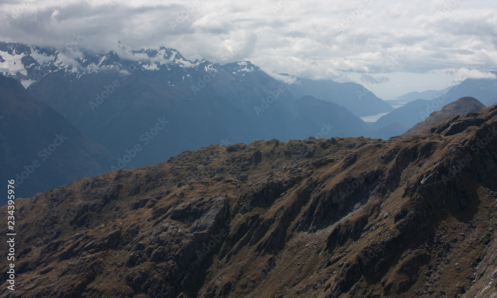 Mountains, Lake Mckerrow and Tasman Sea in the distance as seen from the top of the Conical Hill at Harris Saddle at the Routeburn Great walk in Fiordland, New Zealand