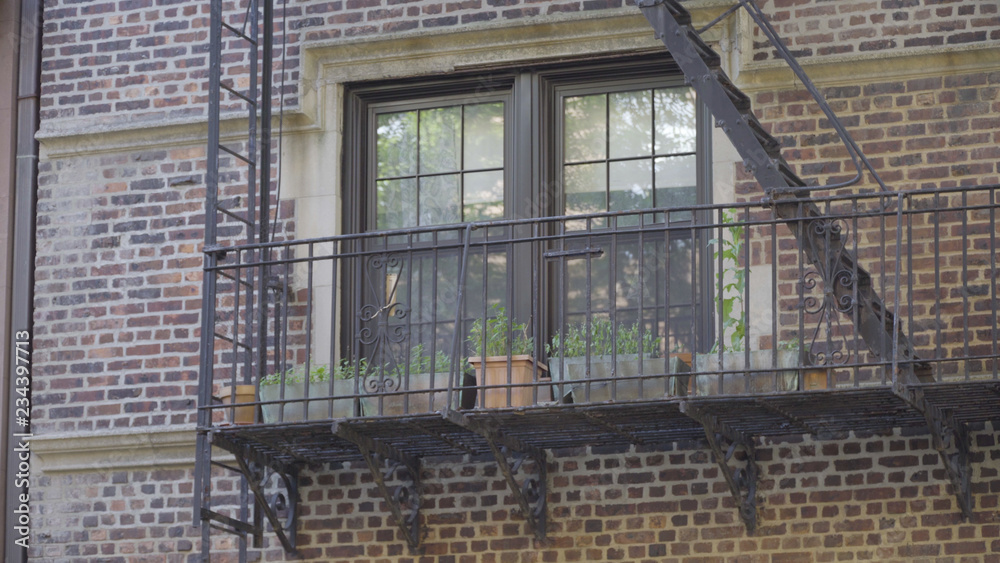 Exterior establishing photo of a generic brick apartment building window along a fire escape. New York City Brooklyn Queens standard structure setting. Day DX outside