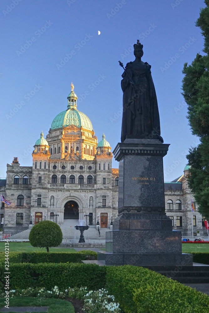 Victoria, British Columbia, Canada: The British Columbia Parliament Buildings (1897), at sunset, with the silhouette of the statue of Queen Victoria in the foreground, and the moon overhead.