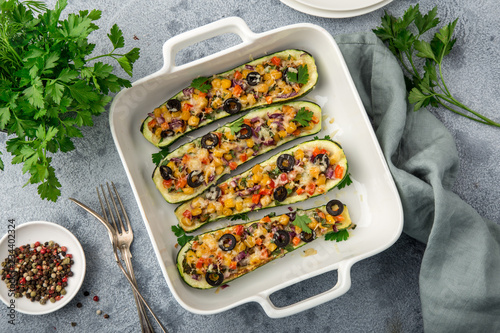 Stuffed zucchini boats with vegetables ( tomato, pepper, corn, red onion and olives) and cheese in white baking dish