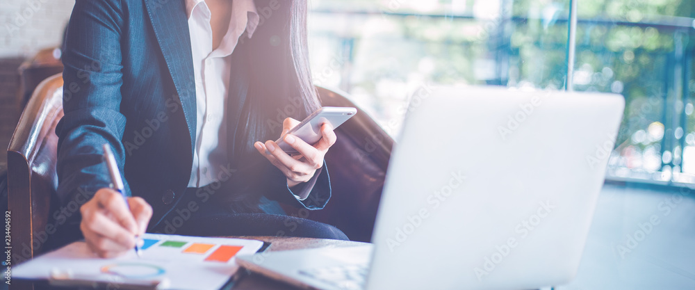 Business woman uses a smartphone and writing on charts and graphs that show results.
