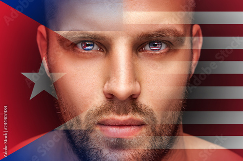A portrait of a young serious man, in whose eyes are reflected the national flags of America and Cuba, against an isolated black background and flag photo