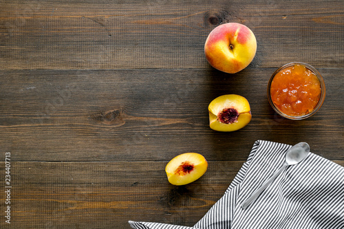 Fruit dessert. Peach jam in jar near slices of fresh peaches and spoon on dark wooden background top view copy space