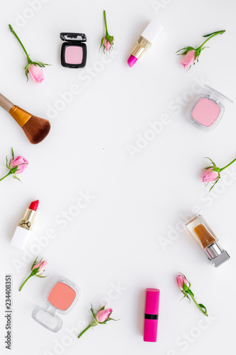 Rose, pink decorative cosmetics frame. Lipstick, bulk, eyeshadow and small rose flowers on white background top view space for text