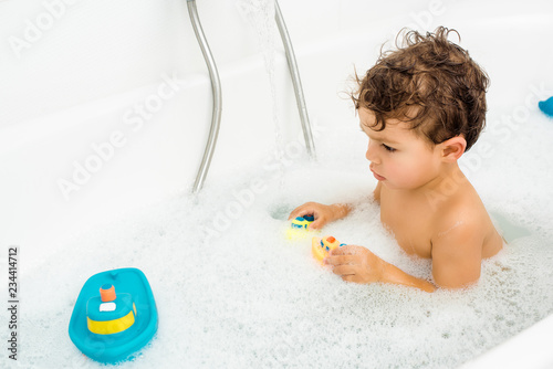 Toddler boy playing with bath toys in white bathroom