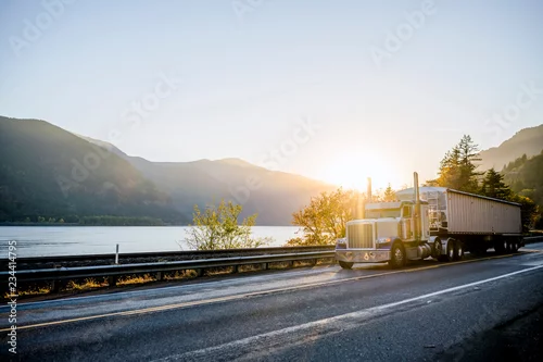 Obraz Klasyczna naczepa typu big rig z naczepą luzem jadąca po drodze wzdłuż rzeki w świetle słonecznym