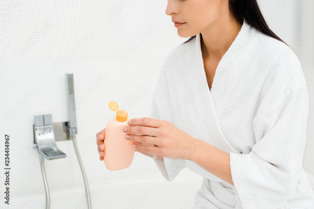 Woman holding bottle with lotion in white bathroom Woman holding bottle with lotion in white bathroom