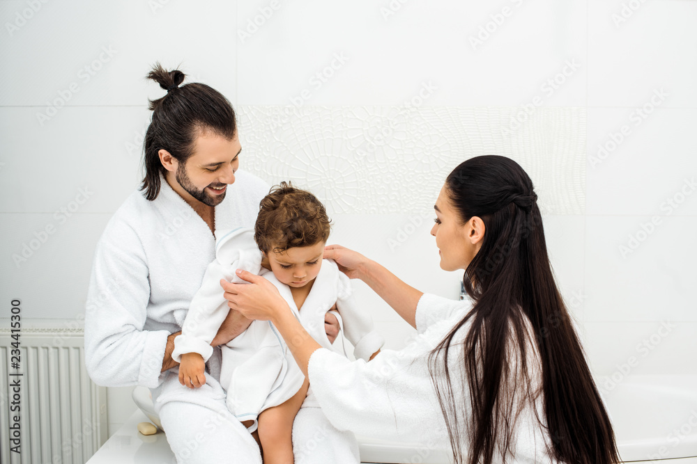 Parents smiling and looking at toddler son in white bathrobe Parents smiling and looking at toddler son in white bathrobe