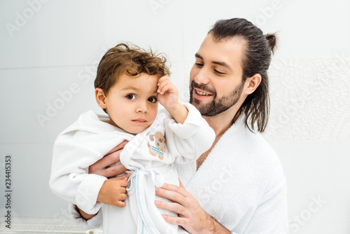 Father holding son in white bathrobe and smile