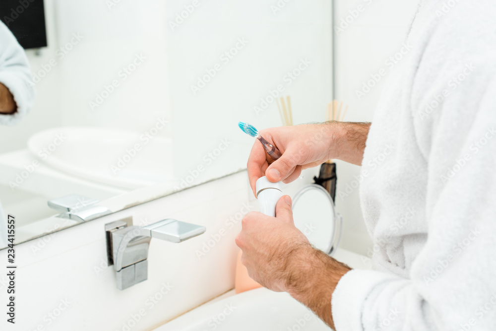 cropped view of male hands holding toothpaste and toothbrush in bathroom cropped view of male hands holding toothpaste and toothbrush in bathroom