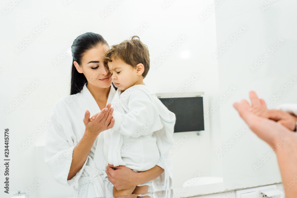 Fototapeta premium mother in white bathrobe gently holding son hand