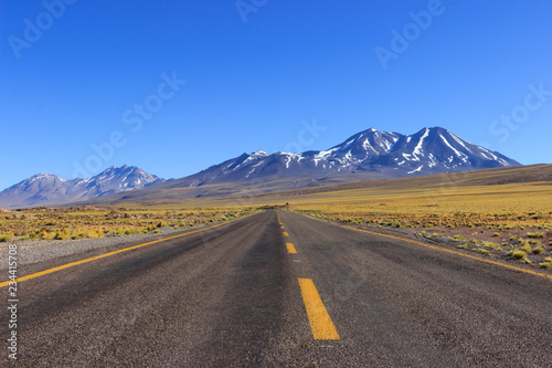 Long road with yellow lines going trough the beautiful view of mountains with snow at the Atacama Desert, Chile, South America