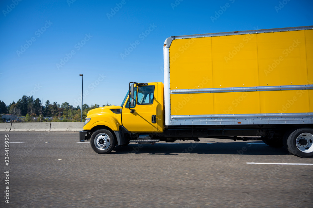 Small rig yellow semi truck with long box trailer running on the highway in city limit Stock