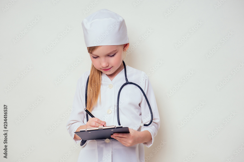 smiling little girl in doctor uniform with medical tools stethoscope writing something to clipboard on white background in studio copy space.future profession vocational guidance career smiling little girl in doctor uniform with medical tools stethoscope writing something to clipboard on white background in studio copy space.future profession vocational guidance career