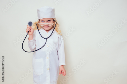 Adorable child girl uniformed as doctor wearing doctor's cap and glasses with stethoscope on white background.Happy kid little female doctor career guidance dreaming about future profession