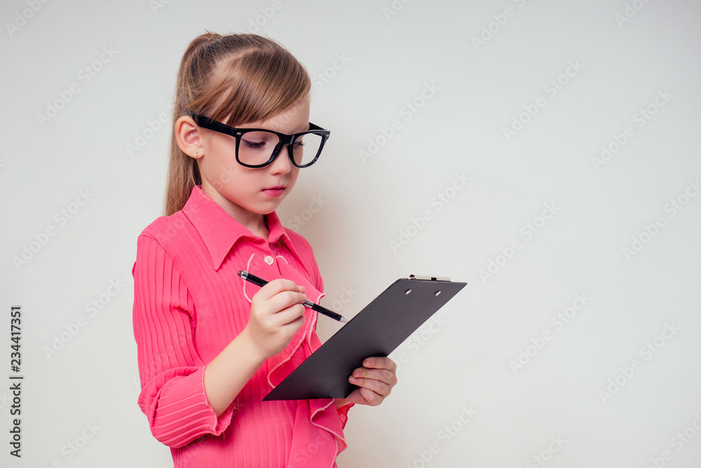 Portrait of thoughtful little smiling girl in a pink blouse and glasses holding notebook and pencil up with tablet copyspace. genius child with the idea on white background in studio copy space