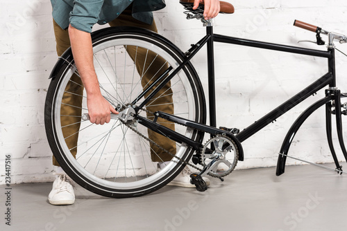 cropped image of young man repairing bicycle by adjustable spanner