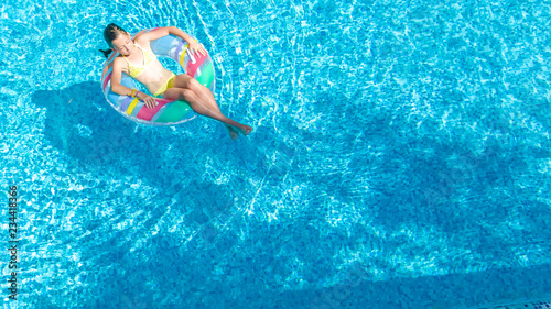 Aerial drone view of little girl in swimming pool from above, kid swims on inflatable ring donut , child has fun in blue water on family vacation resort 