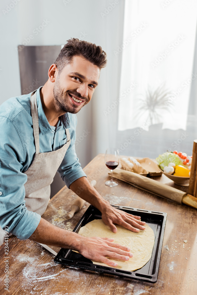 smiling young man in apron preparing pizza dough on baking tray Stock Photo  | Adobe Stock