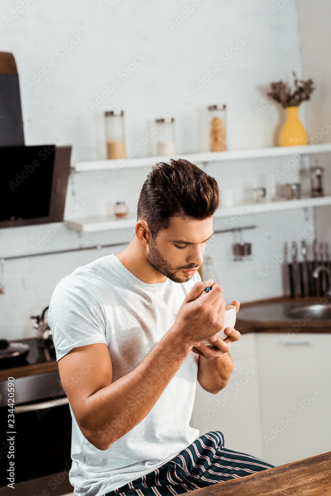 high angle view of young man in pajamas eating cereals for breakfast at home high angle view of young man in pajamas eating cereals for breakfast at home