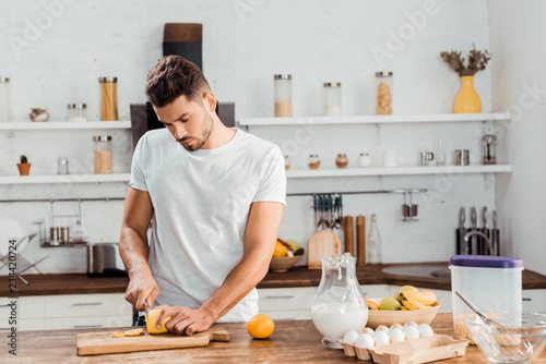 handsome young man cutting lemon on chopping board in kitchen