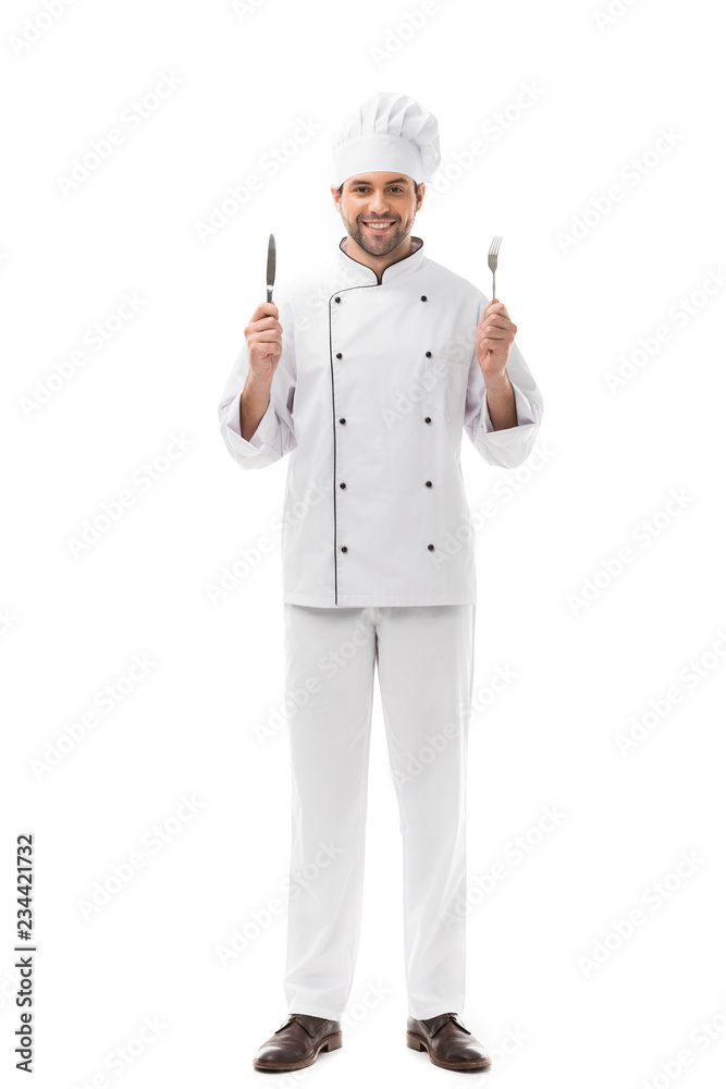 smiling young chef holding knife and fork and looking at camera isolated on white