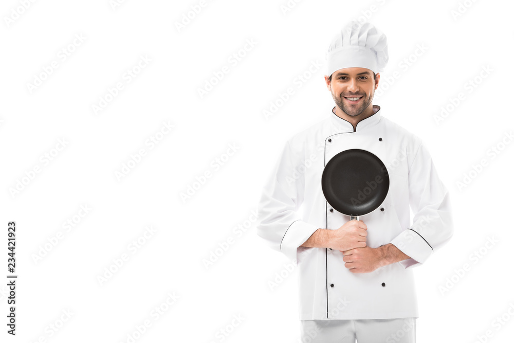 happy young chef holding frying pan and looking at camera isolated on white
