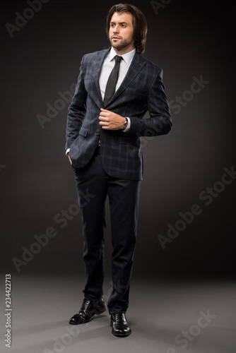 full length view of professional serious businessman in stylish suit looking away on black