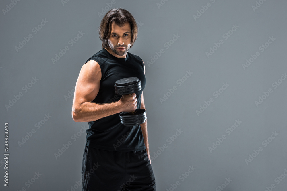 handsome athletic man holding dumbbell and looking at camera isolated on grey handsome athletic man holding dumbbell and looking at camera isolated on grey