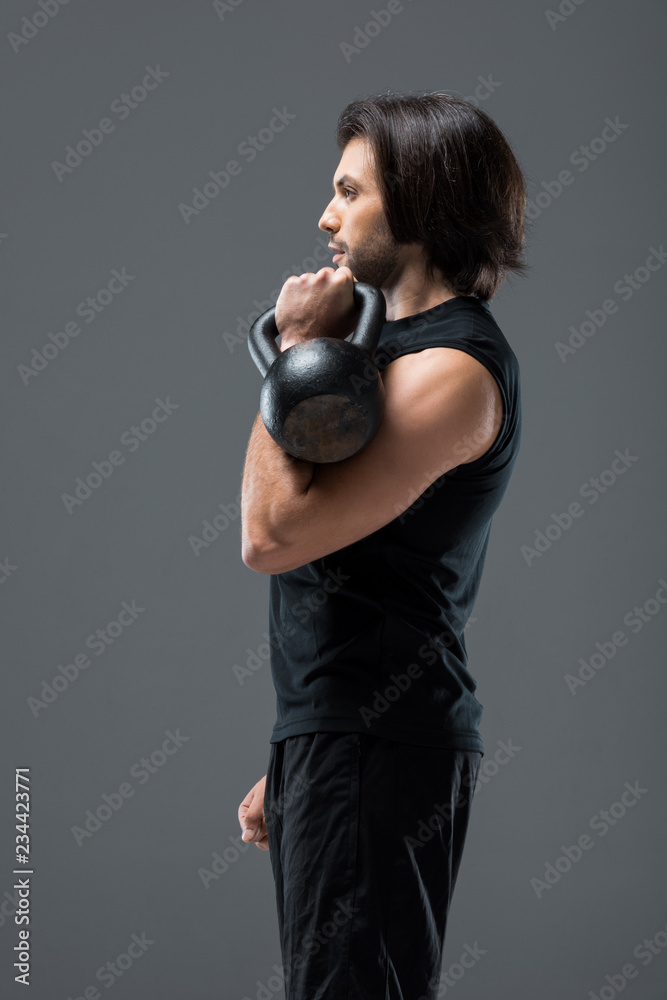 Fototapeta premium side view of muscular young man exercising with kettlebell isolated on grey
