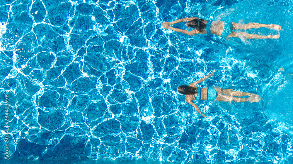 Active girls in swimming pool water aerial drone view from above, children swim, kids have fun on tropical family vacation, holiday resort concept
