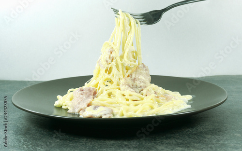 Spaghetti Carbonara in a Brown plate with Bacon and milk line yellow on a stone floor table,Close up a hand is using a fork to fetch spaghetti.. photo