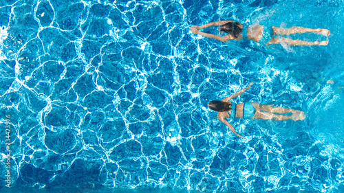 Active girls in swimming pool water aerial drone view from above, children swim, kids have fun on tropical family vacation, holiday resort concept
