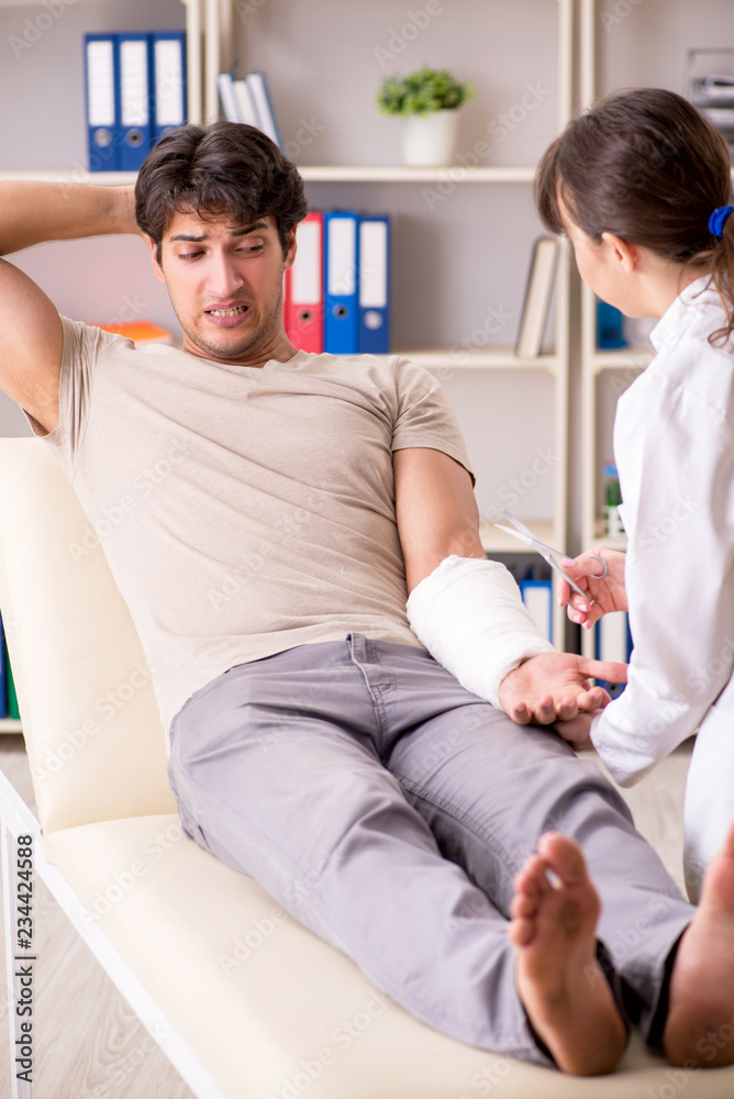 Fototapeta premium Young man with bandaged arm visiting female doctor traumatologis