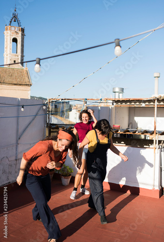 Gorgeous Hispanic women dancing synchronically standing outdoors at old shabby buildings and laughing on sunny summer day photo