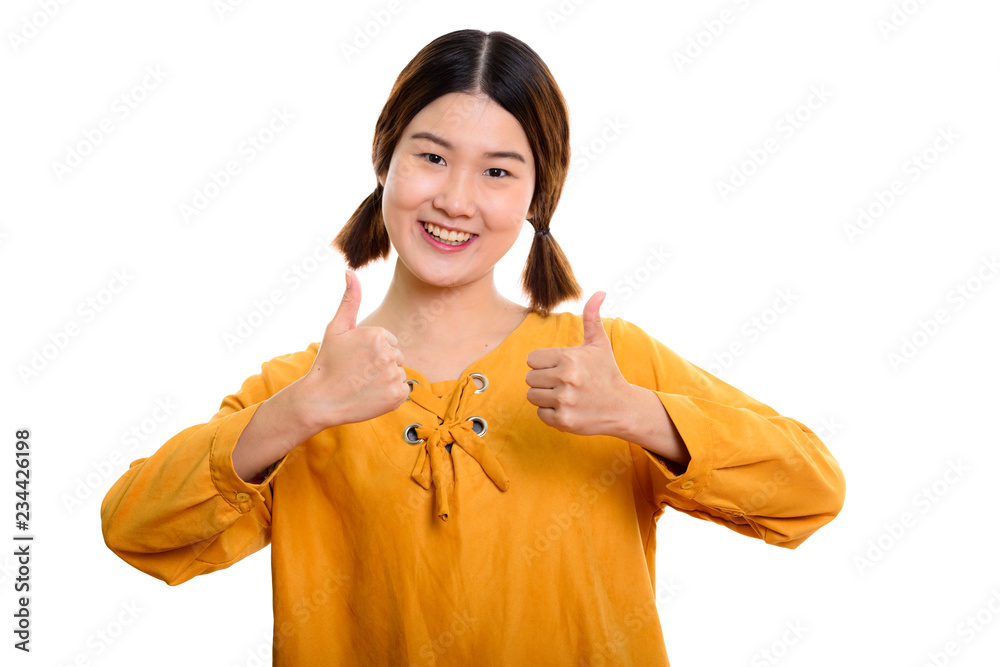 Studio shot of young happy Asian woman smiling while giving thum Studio shot of young happy Asian woman smiling while giving thum