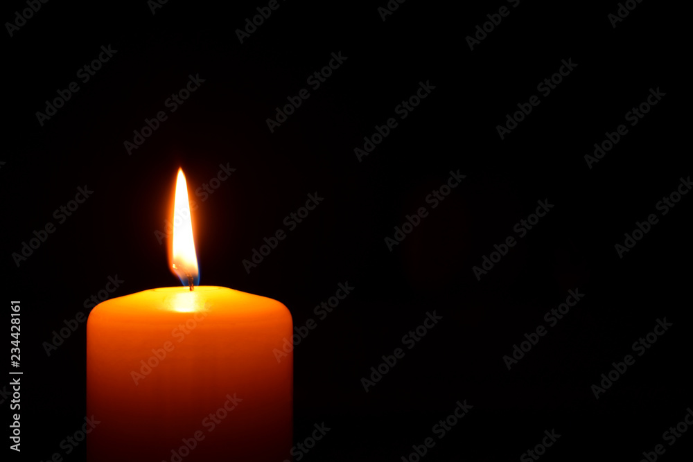 One orange candle flame burning in darkness on black background with copy space for text. One orange candle flame burning in darkness on black background with copy space for text.