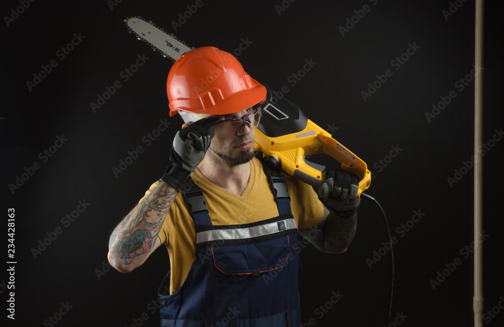 a young man posing on a black background in a work uniform and a construction tool a young man posing on a black background in a work uniform and a construction tool