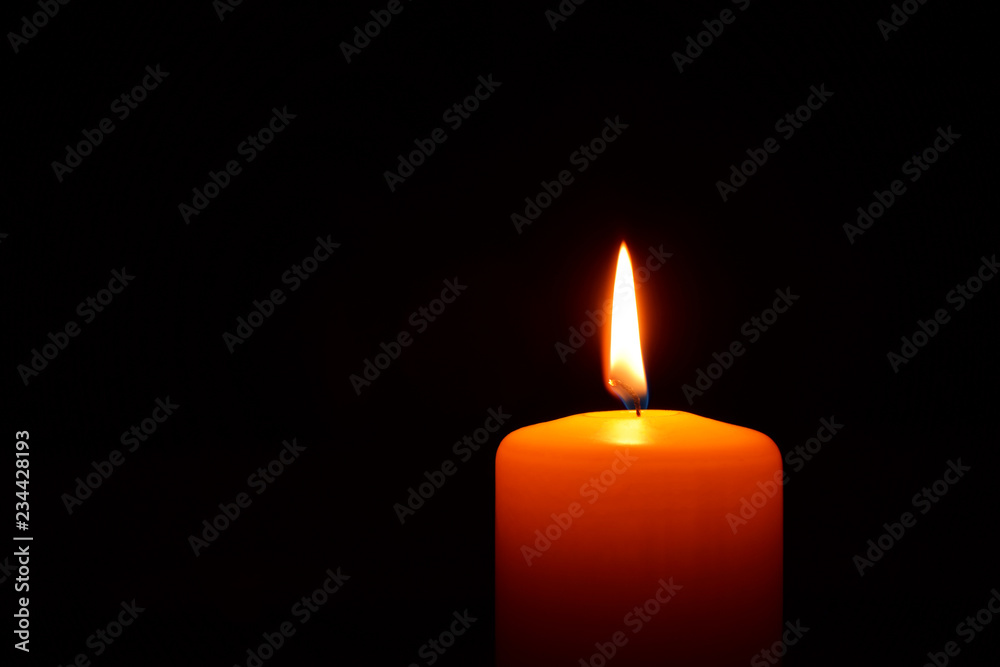 One orange candle flame burning in darkness on black background with copy space for text. One orange candle flame burning in darkness on black background with copy space for text.