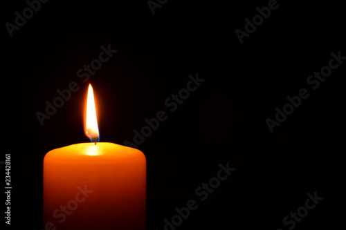 One orange candle flame  burning in darkness on black background with copy space for text.