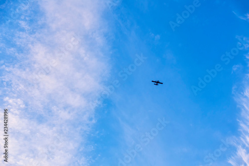 flight of a twin-engine plane high in the sky against a blue sky and clouds