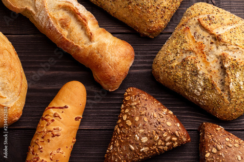 Contrast bread background. Concept for bakery menu. Different color, size and shape of the bread lies on the dark natural pine boards. photo