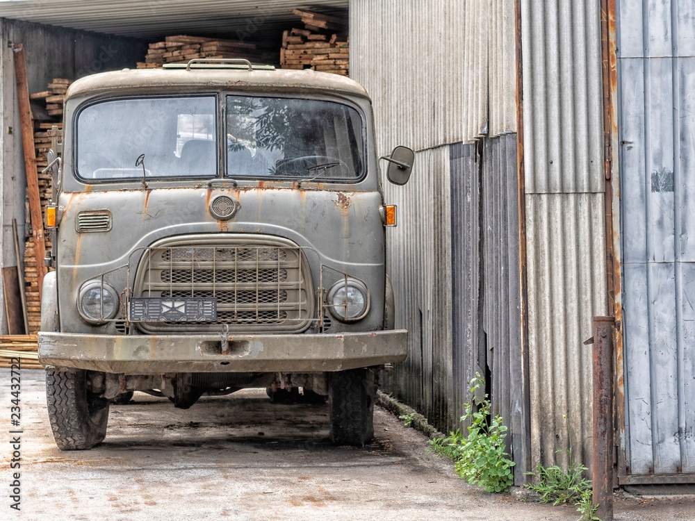 Oldtimer Lastwagen angerostet, steht auf einem Platz neben einem metallenen  Schuppen