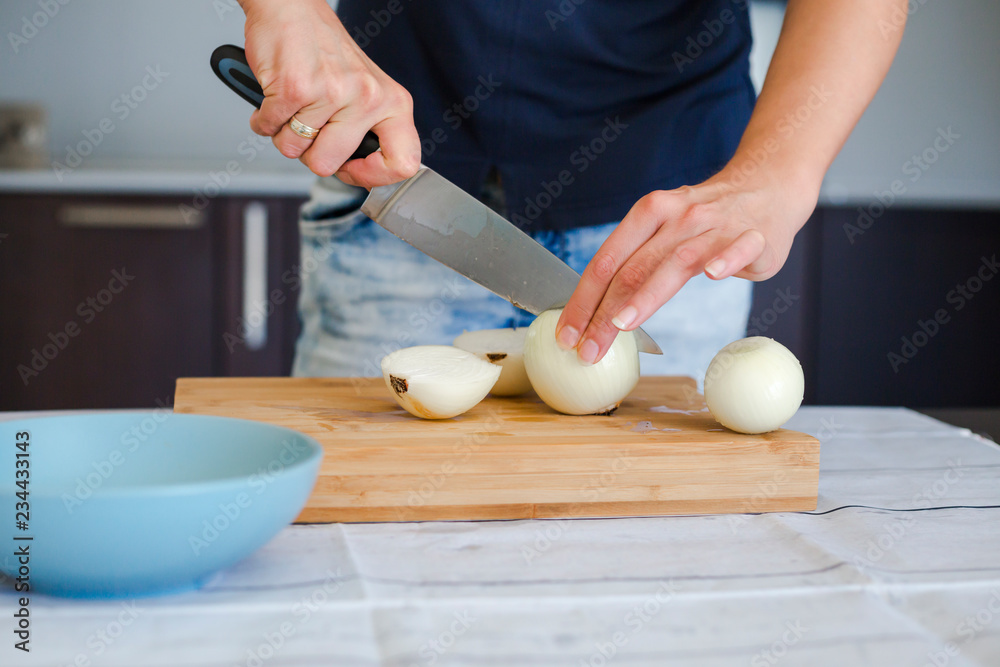 Woman with knife cutting onion on wooden cutting board, close-up Woman with knife cutting onion on wooden cutting board, close-up