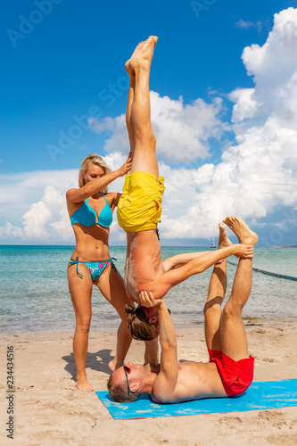 two young man and woman on beach doing fitness yoga exercise together. Acroyoga element for strength and balance
